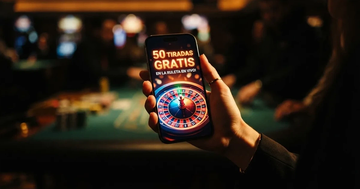 Primer plano de una mano sujetando un móvil con una ruleta de casino y el texto «50 tiradas gratis» en pantalla, sobre un fondo oscuro con luz cálida.